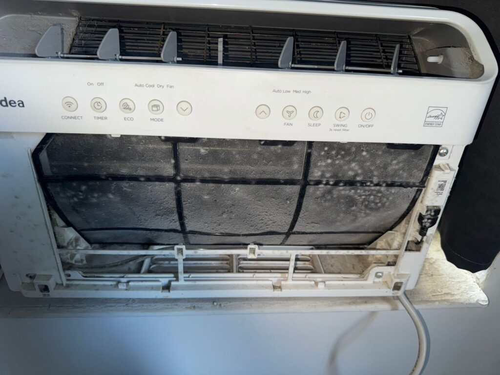 Dirty window air conditioner in NYC apartment with heavy dust buildup and clogged vents